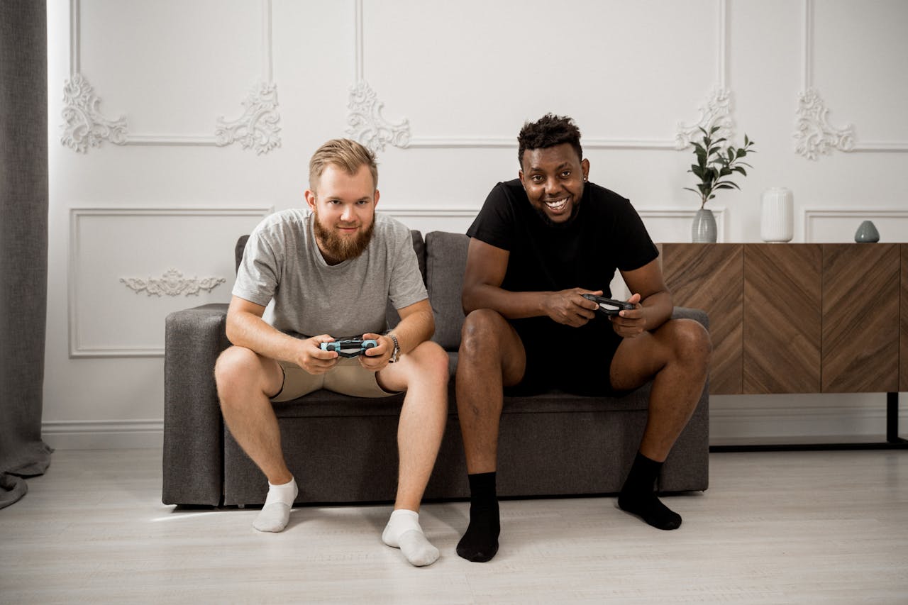 Two diverse men happily playing video games together on a stylish sofa indoors.